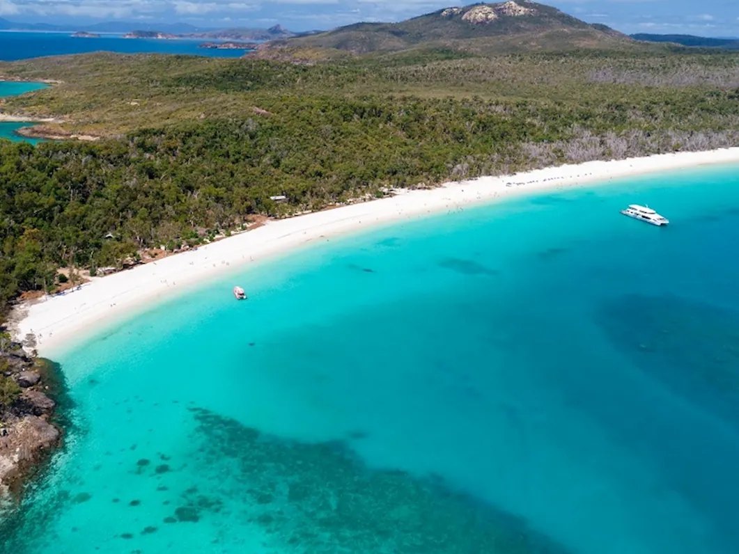 Aerial view of the southern end of Whitehaven Beach, with the day-use and camping area in the trees behind the sand and boats anchored offshore, Whitsunday Island
